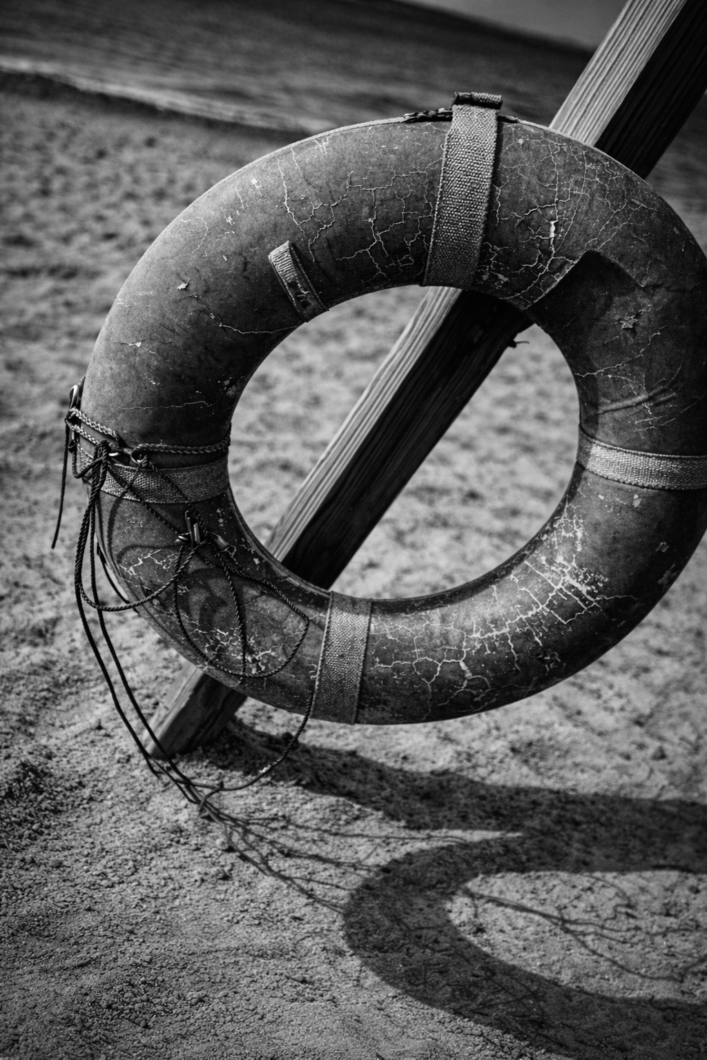 Weathered life preserver on beach post — cracked texture, strong shadow, fine art black and white photography by Craig Moyers