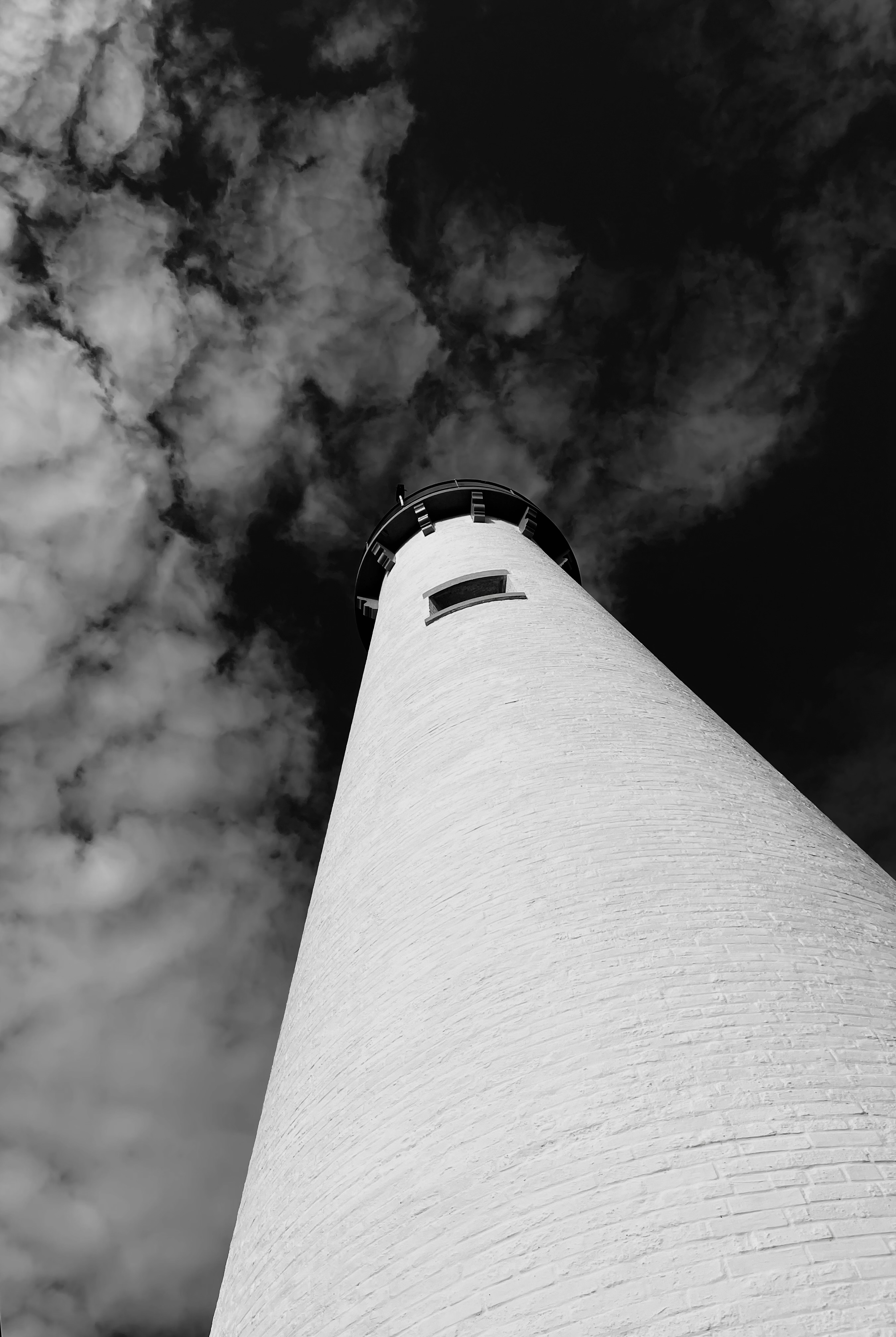Lighthouse at dramatic low angle — white structure against dark clouds, fine art black and white landscape photography by Craig Moyers