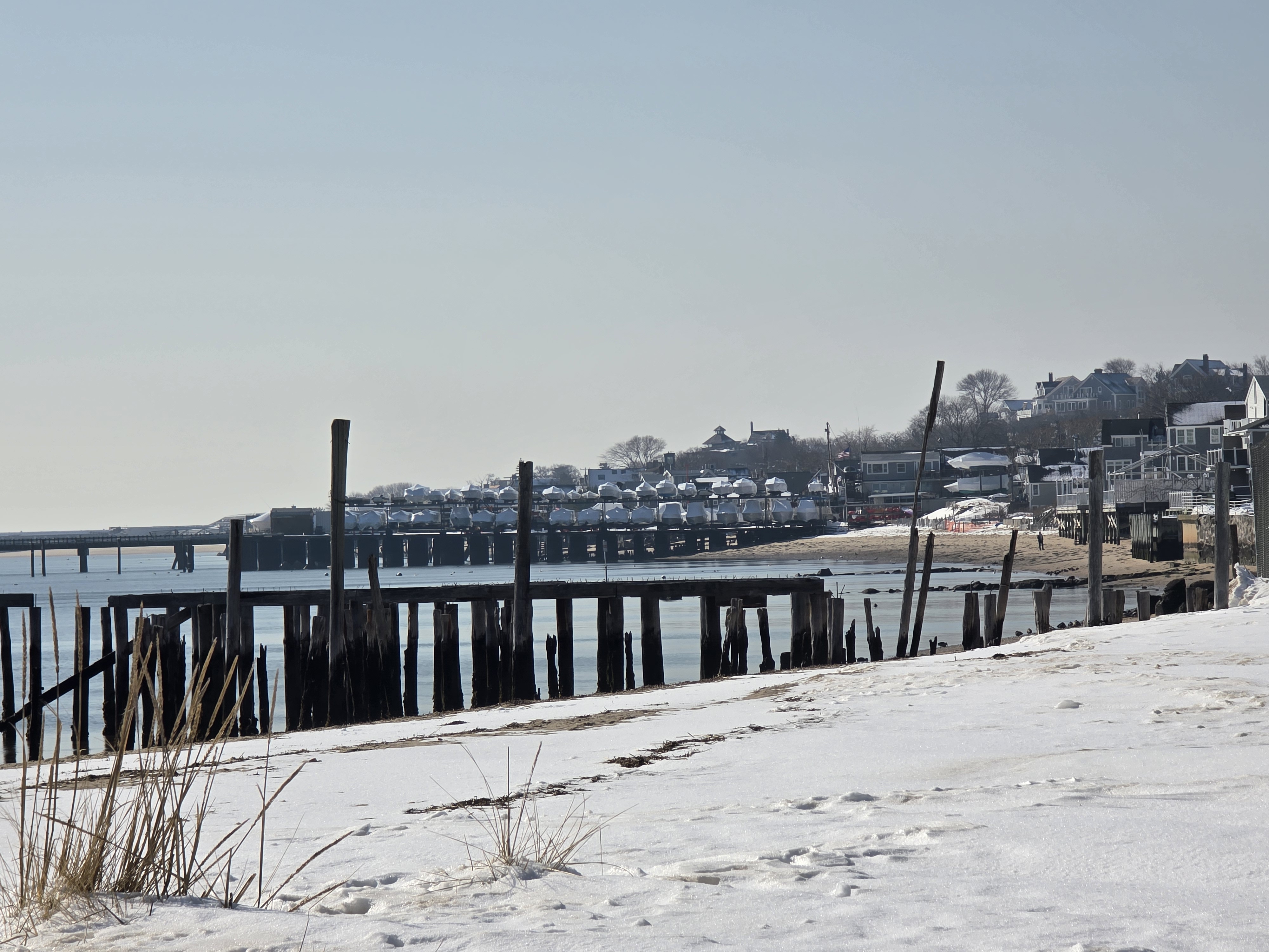 Winter Provincetown harbor — snow-covered shore, weathered pilings, boats in storage