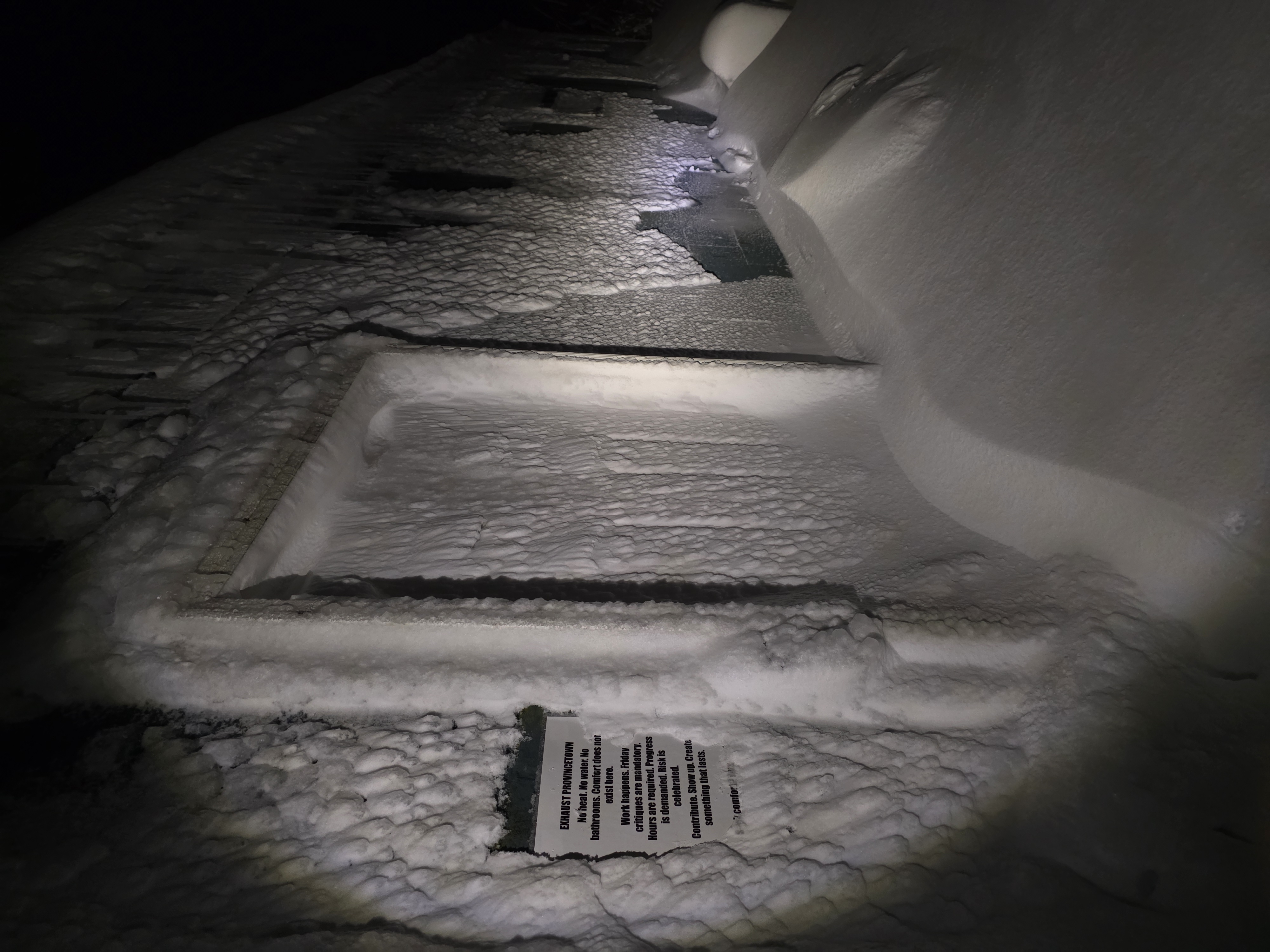 Studio exterior buried in snow during a blizzard, manifesto posted on wall beside door