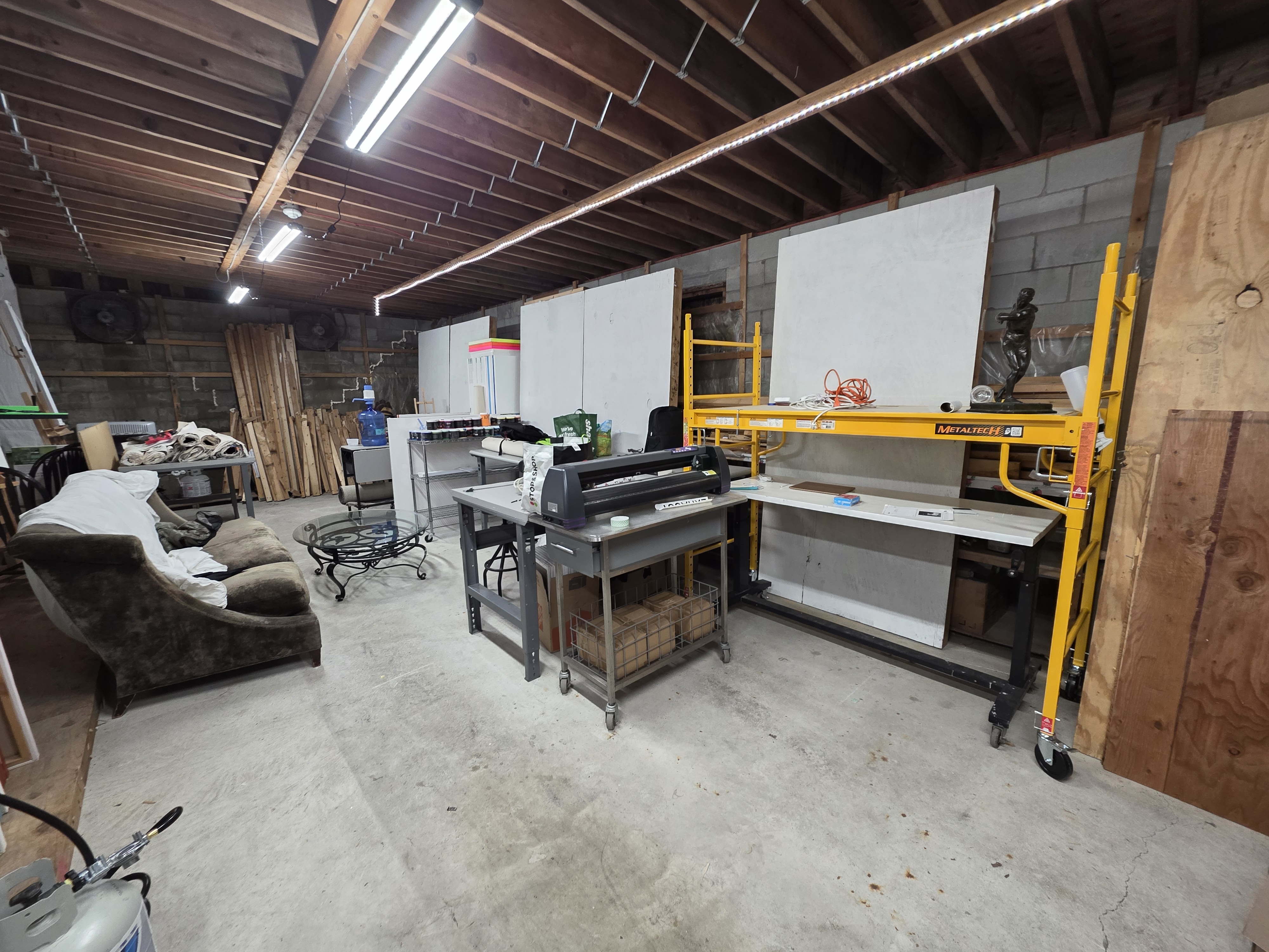 Studio interior — cinder block walls, concrete floor, blank canvases, scaffolding, work tables