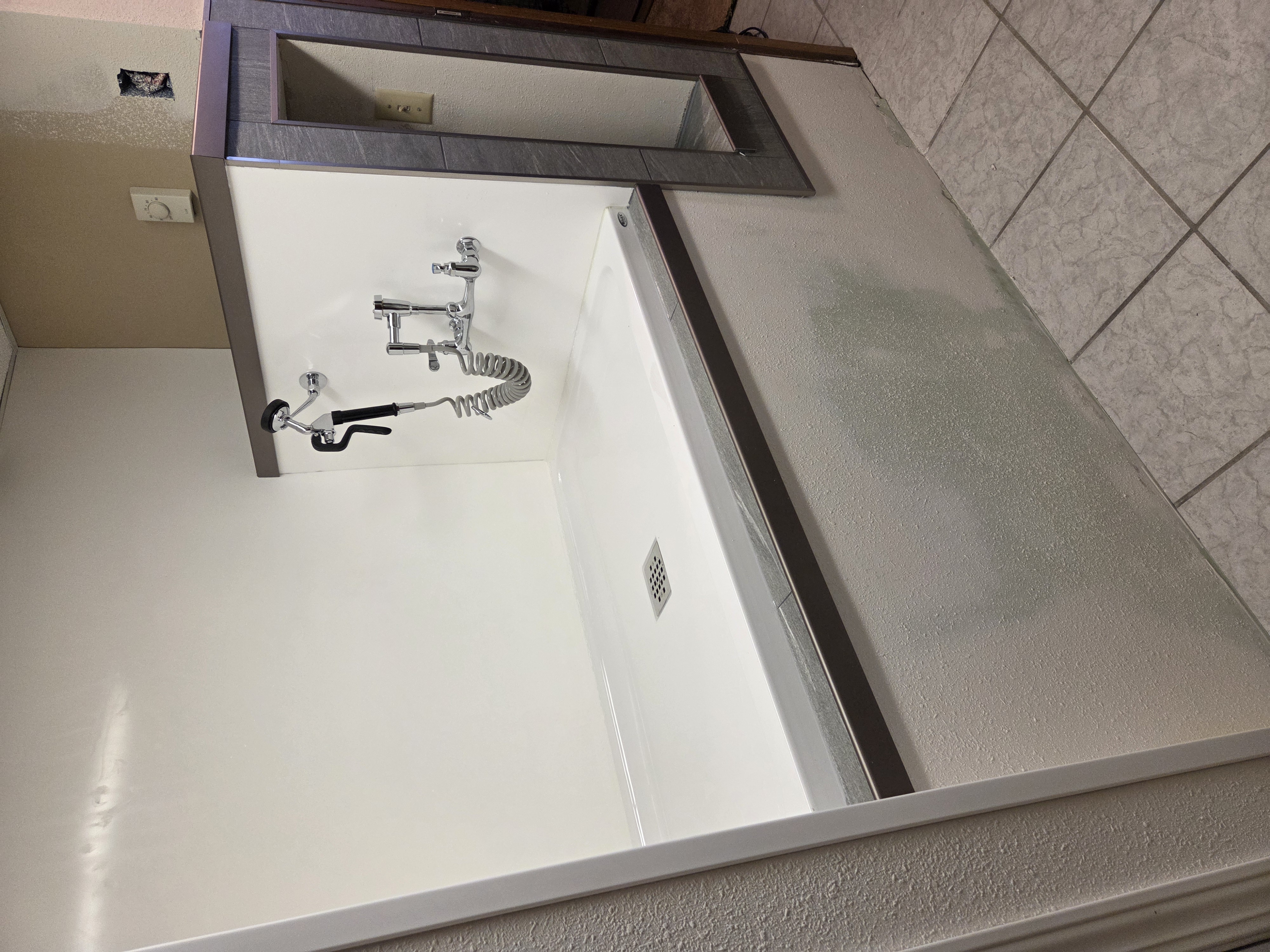 Completed dog wash station — full alcove, pan, sprayer, tile-framed pass-through, half-wall