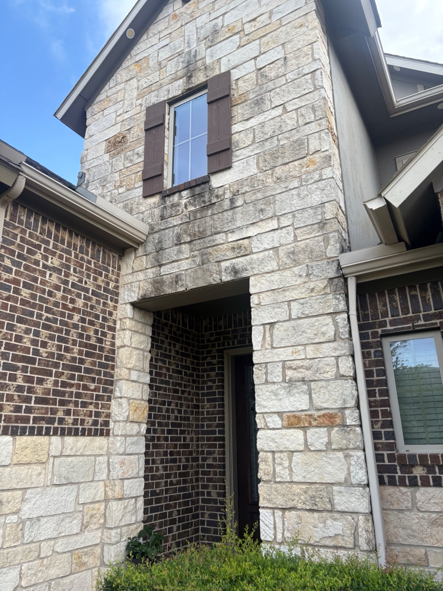 Stone and brick home before washing — stained entry with mildew and algae buildup