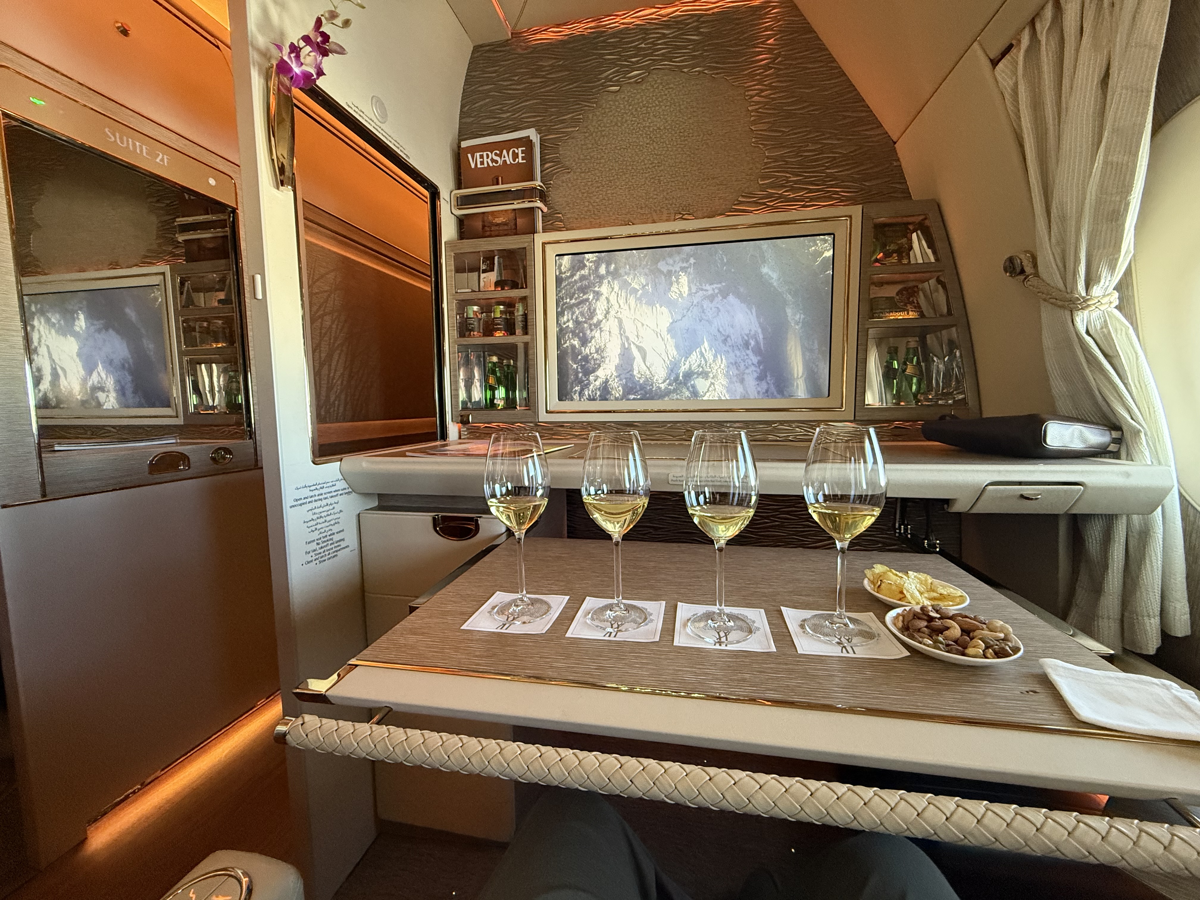 Emirates First Class Suite 2F with white wine flight, Versace amenity kit, and mini-bar area