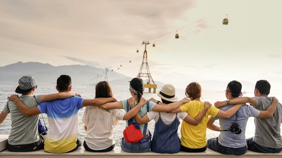 A group of friends and family sitting together with arms around each other, enjoying a golden-hour view of the ocean, cable cars, and mountains