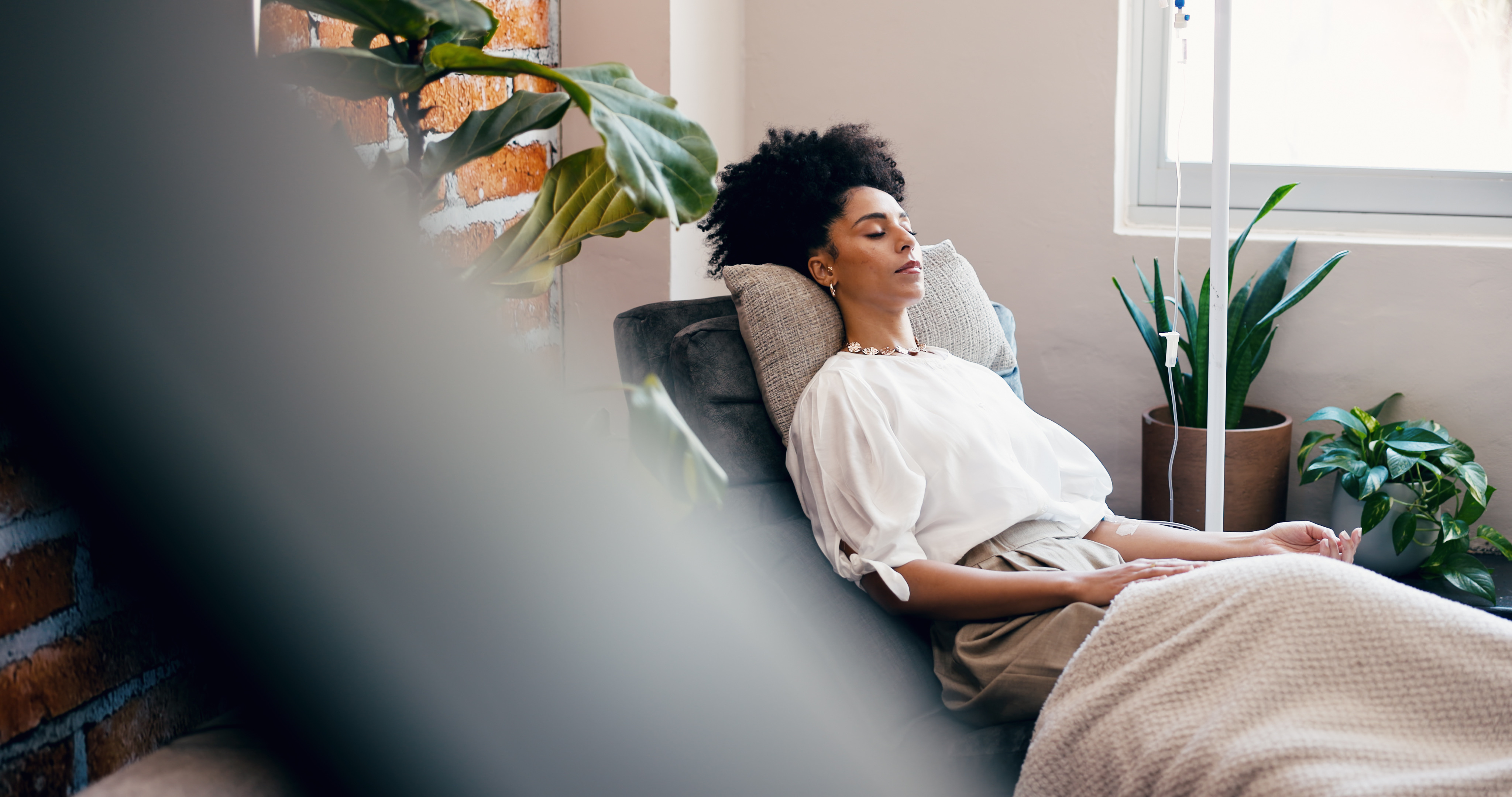 Woman relaxing in premium IV therapy lounge with plants and cozy atmosphere
