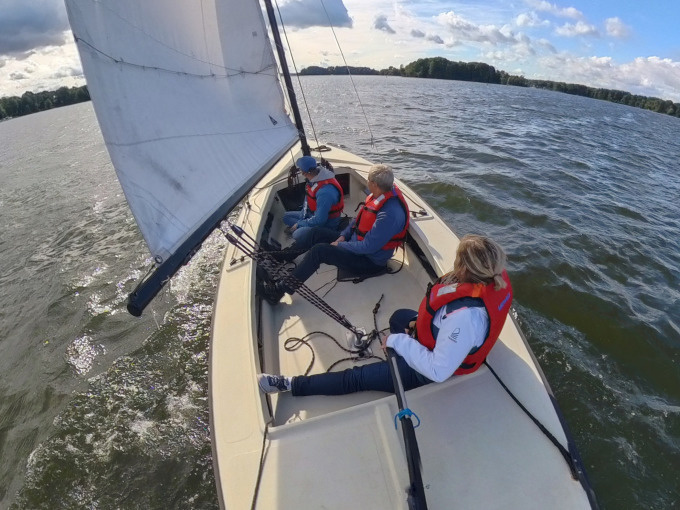 Gruppe beim Segeln – 3 Personen mit Schwimmwesten auf der Kieljolle
