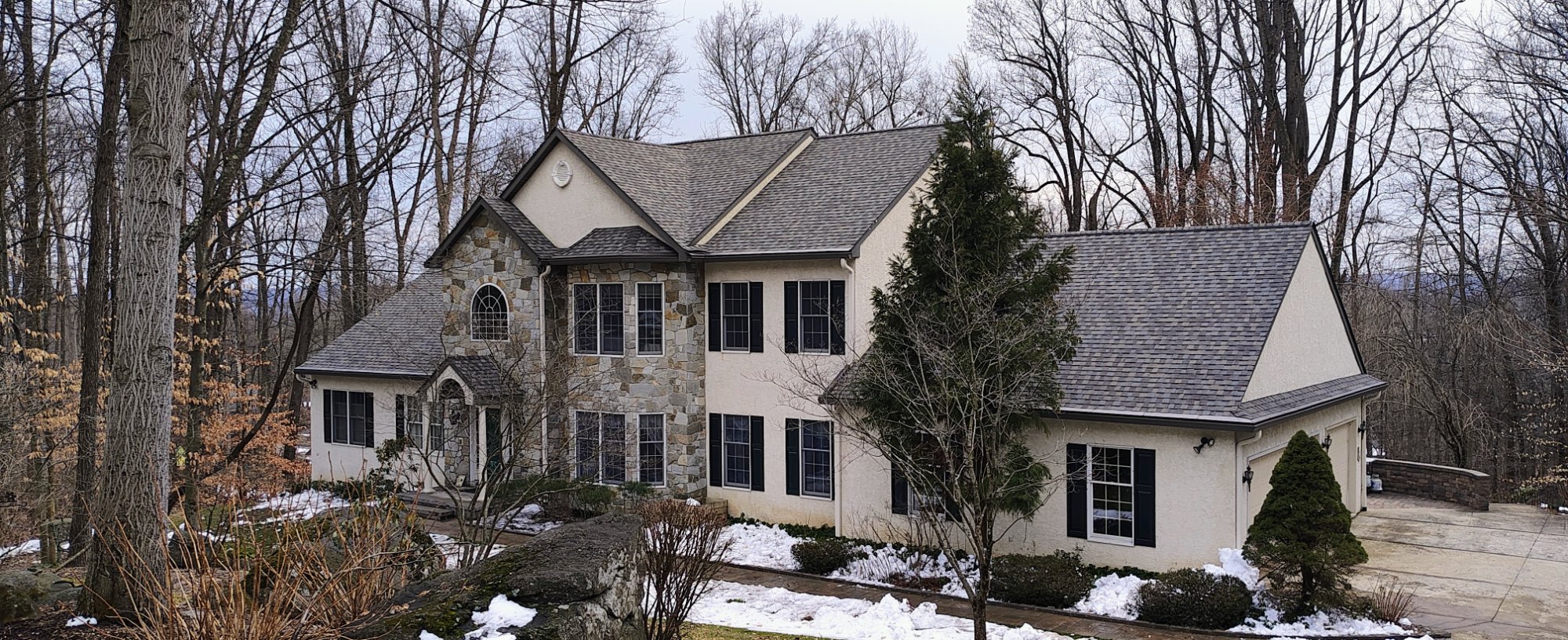 Large stone and stucco estate home with new gray architectural shingles — completed roof replacement in Pennsylvania, winter scene