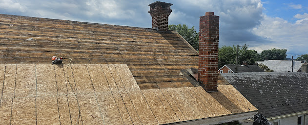 Wide view of full roof deck repair — complete OSB sheathing replacement across entire roof with two chimneys visible