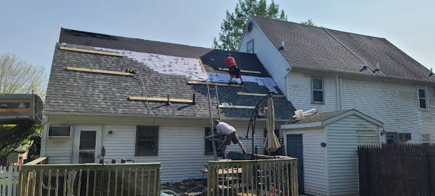 Two crew members working mid-install on Cape Cod roof — underlayment and new shingles visible from ground view
