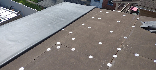 EPDM flat roof installation in progress — insulation board with mechanical fasteners being installed on flat roof deck