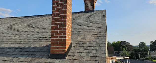Close-up of new architectural shingles around brick chimney — clean professional flashing detail at penetration