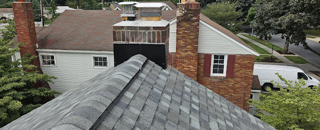 Finished shingles rooftop view showing chimney and ridge cap from above — clean install across full pitch