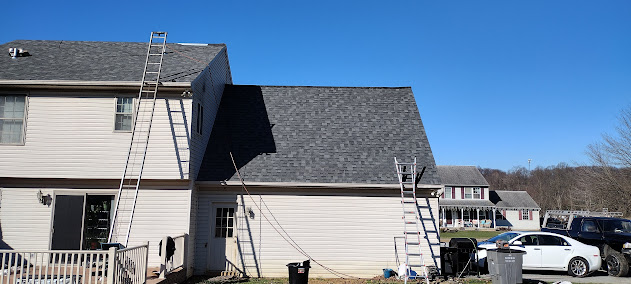 Mid-install full shingle roof replacement — multiple ladders on large farmhouse against blue sky