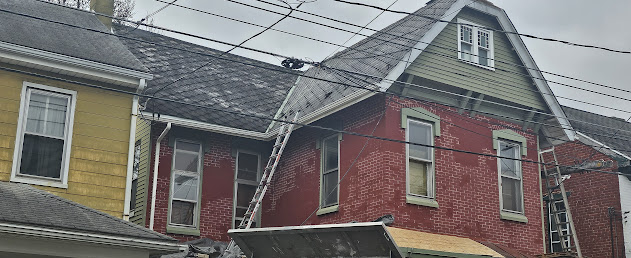Ladders set up for roof tear-off between brick buildings — asbestos shingle removal in progress Lebanon PA