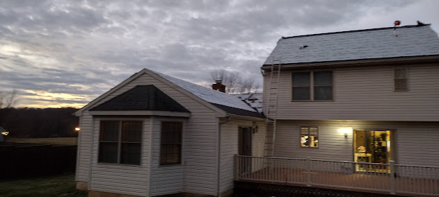 Large farmhouse at dusk with ladder up — roofing crew setting up for full shingle replacement