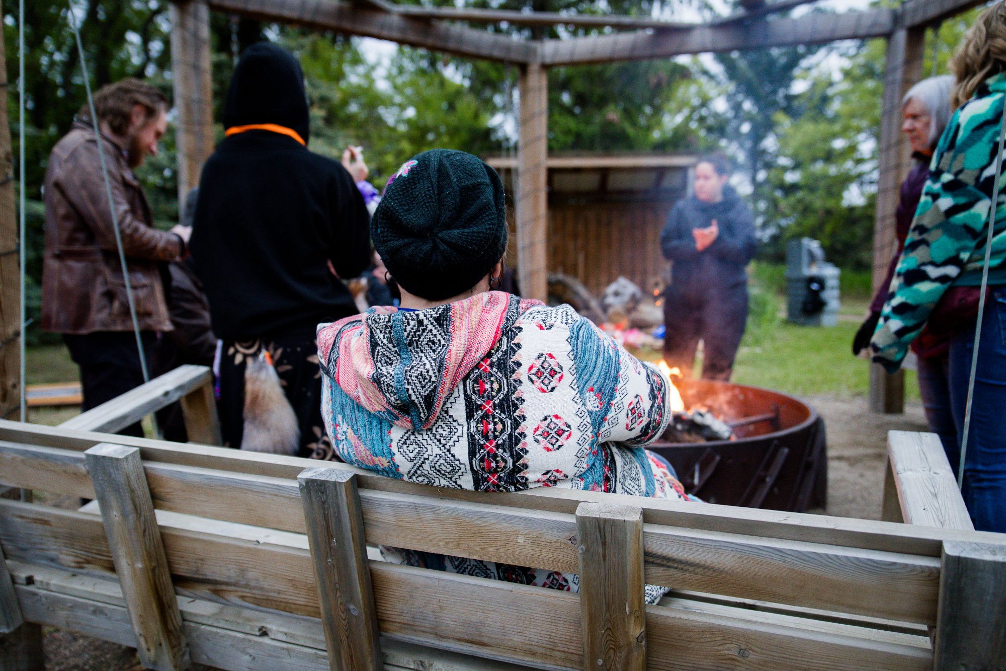 Guest on the wooden swing bench by the fire pit at Wiebe Works — people gathered under the pergola