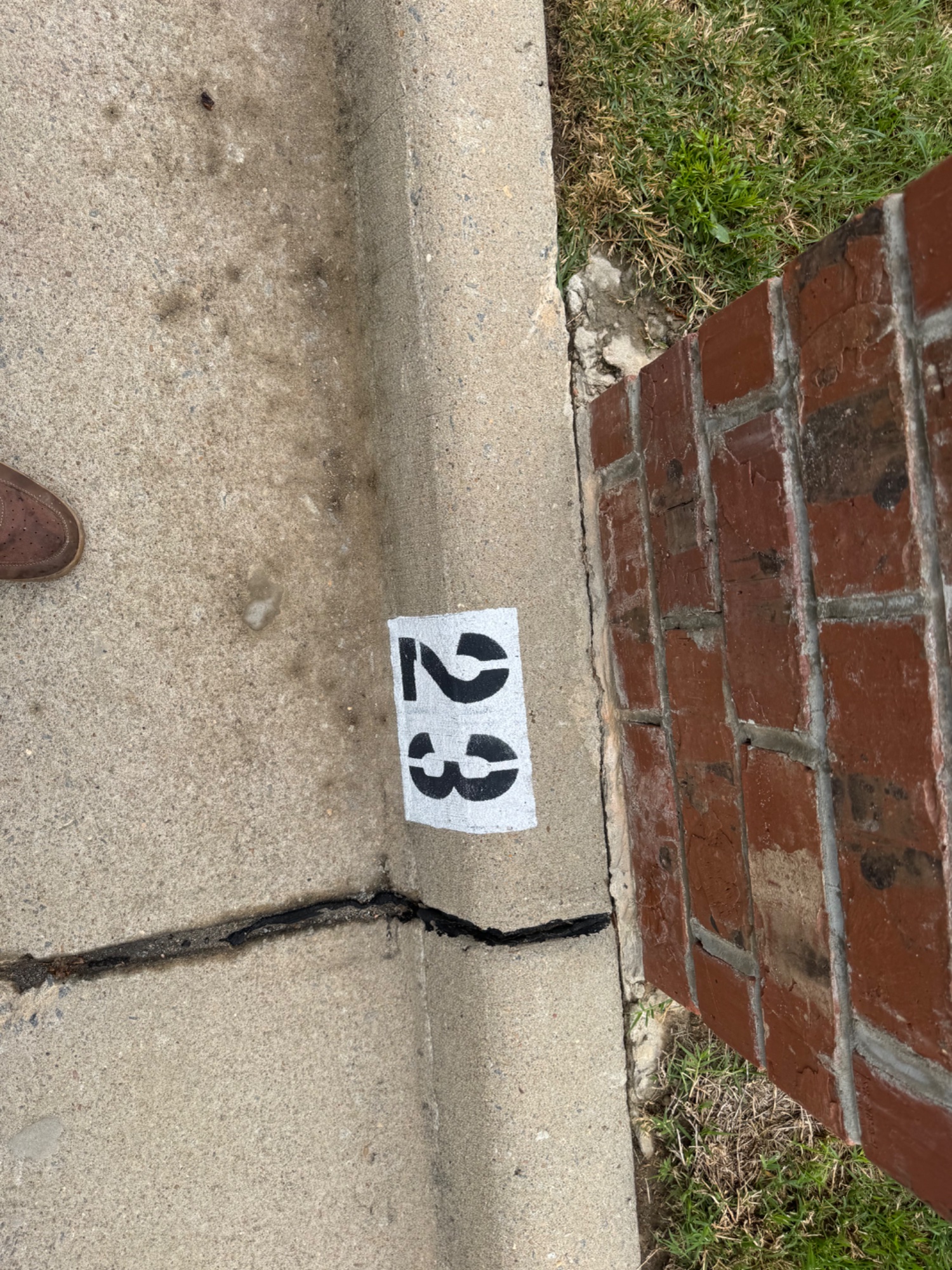 4-digit address painted on sidewalk curb next to brick wall