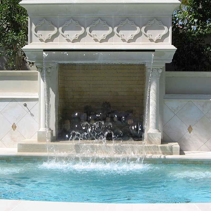 Ornate cast stone outdoor pool fireplace surround with arabesque balustrade cornice detailing and cascading waterfall feature — luxury residential pool design