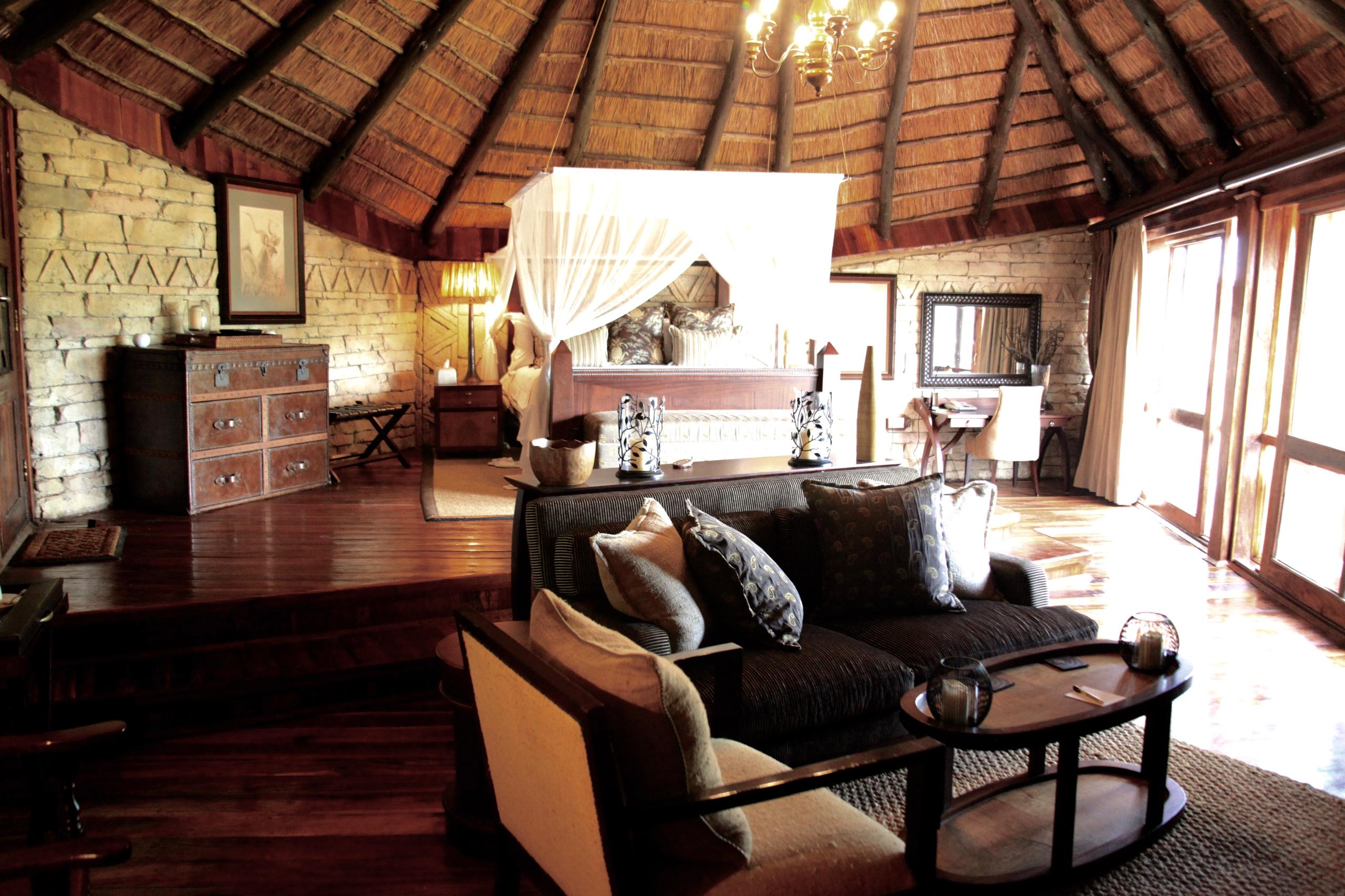 Lodge bedroom — four-poster bed under thatched ceiling, elegant safari accommodation