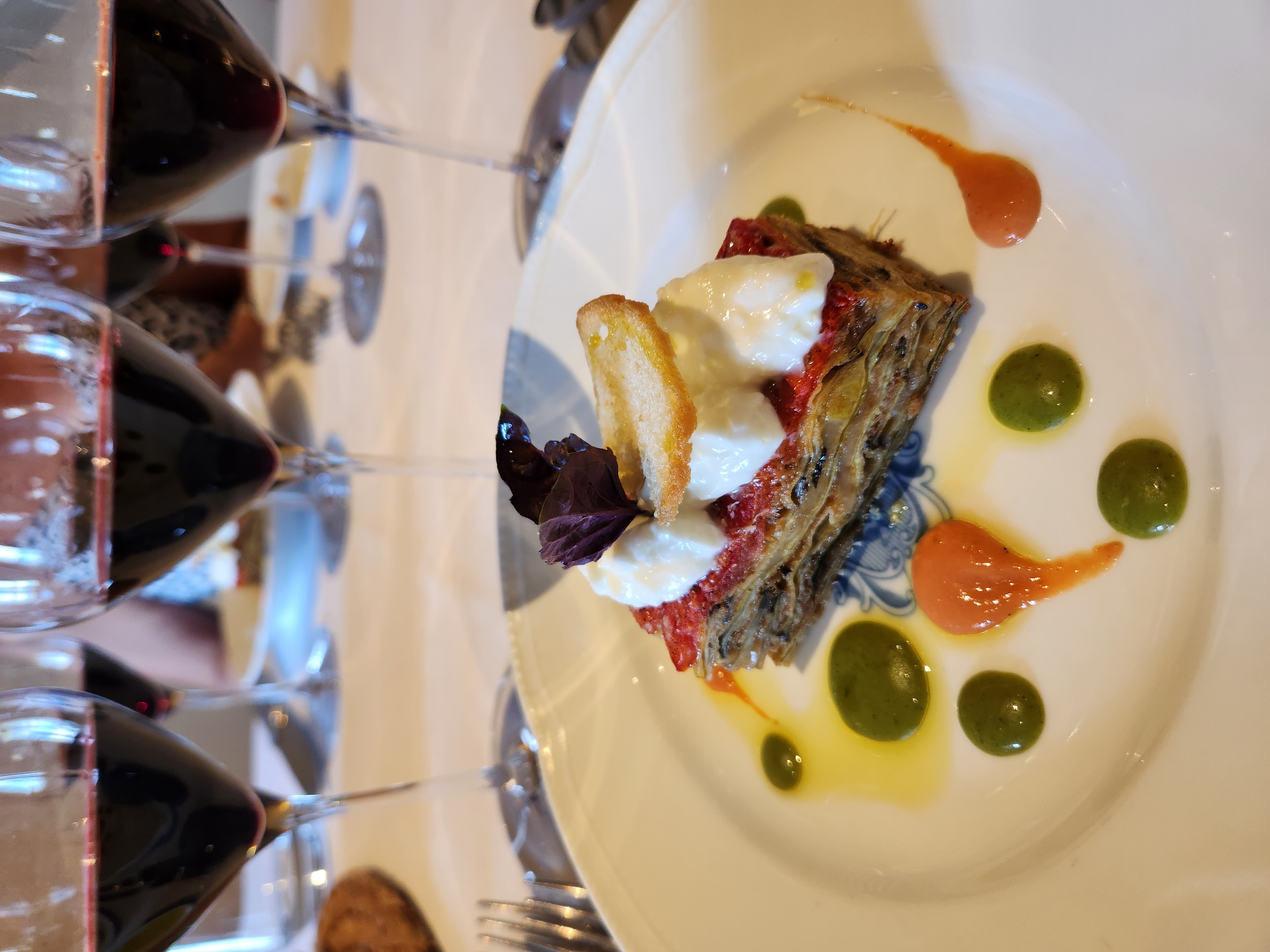 A plated Italian dish with red wine glasses set behind it.