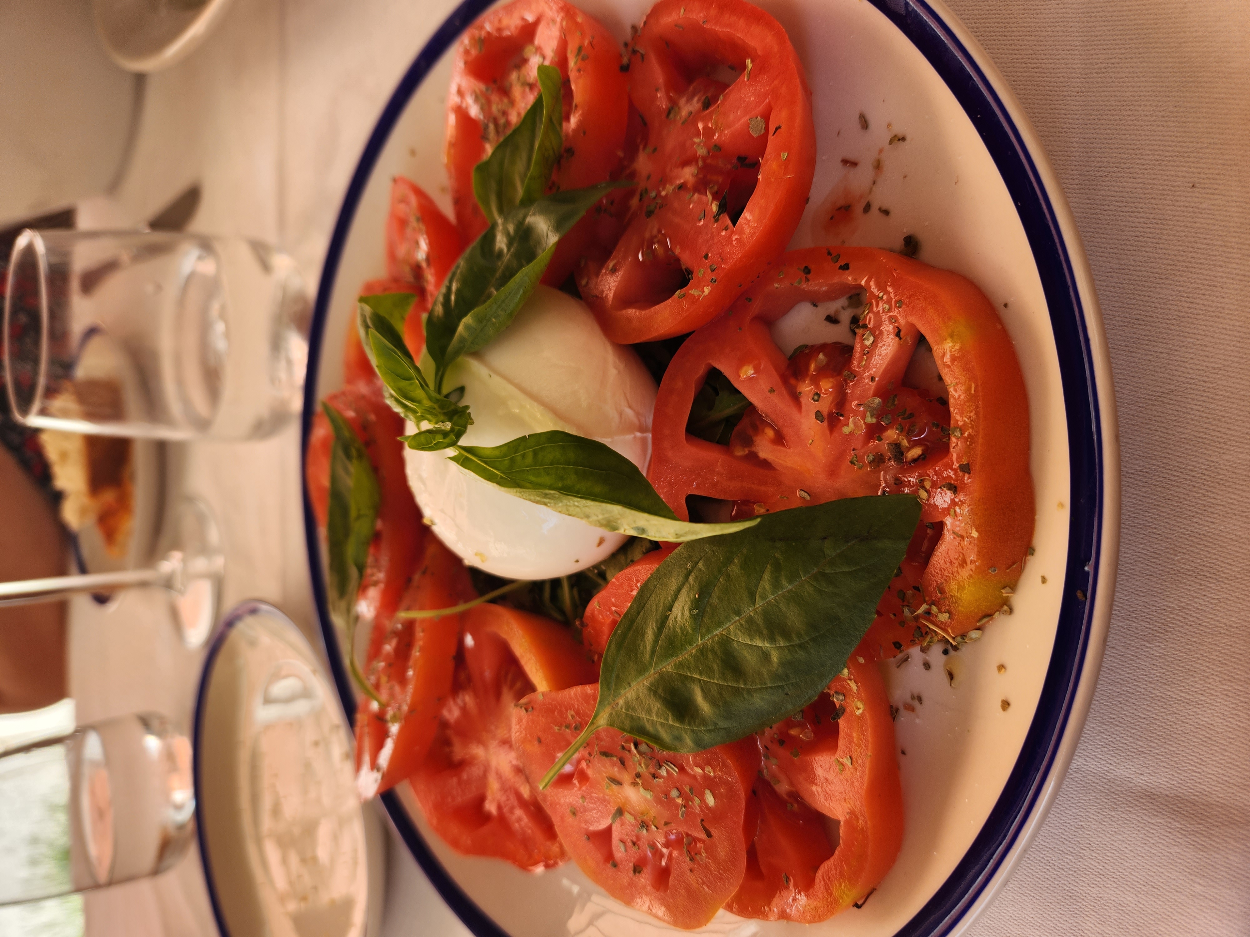 Tomatoes, fresh cheese, and basil arranged on a plate at an Italian table.