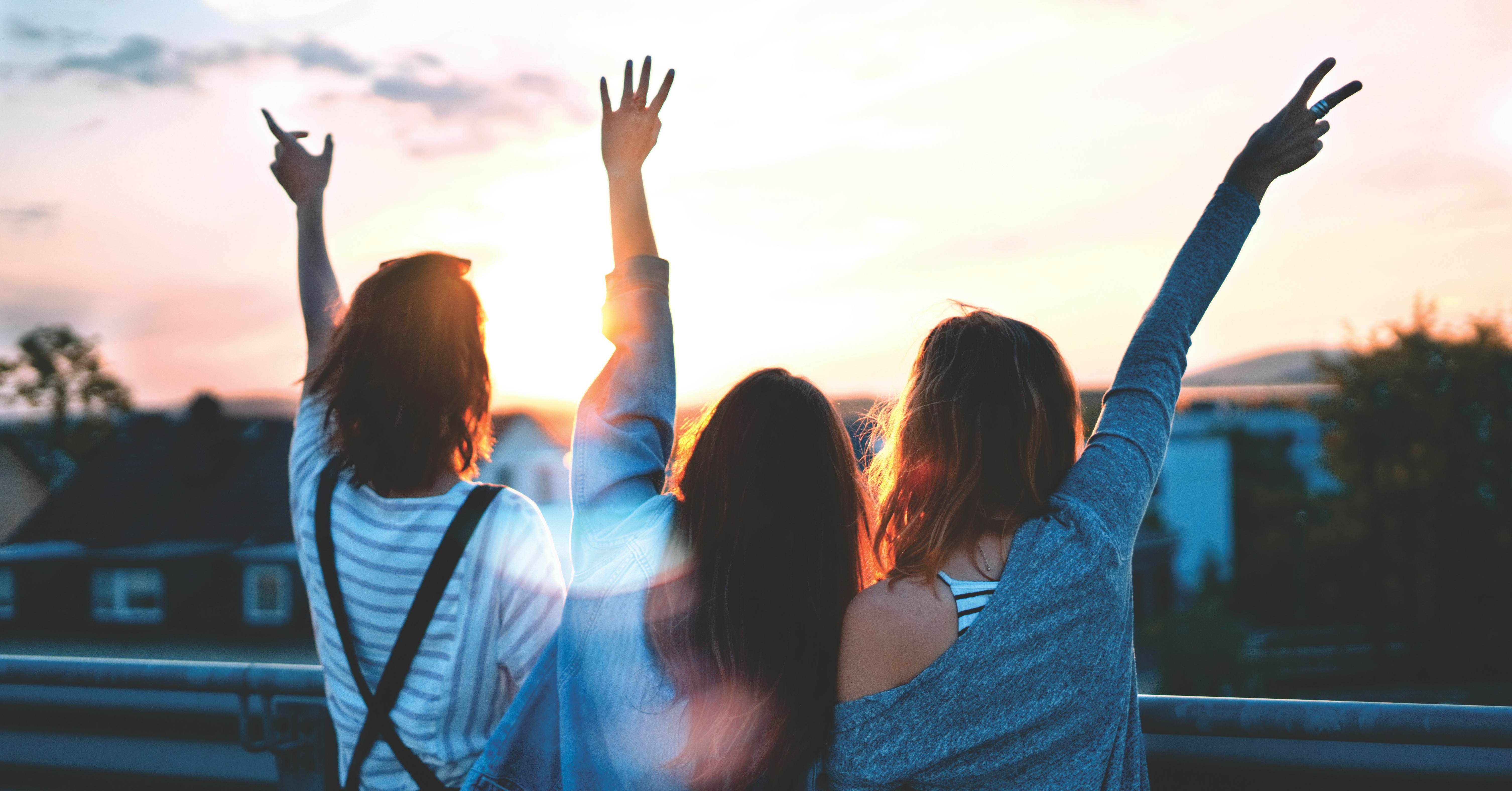 Four friends raising their arms together in the warm light of sunset.