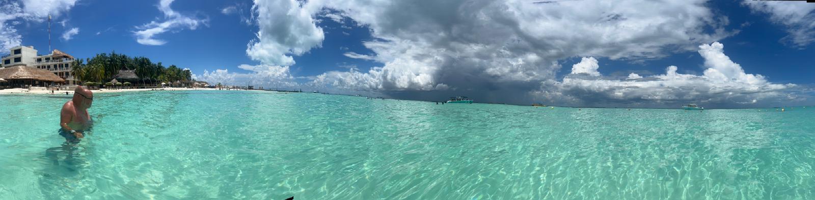 Clear turquoise sea beneath a dramatic sky beside a coastal resort.
