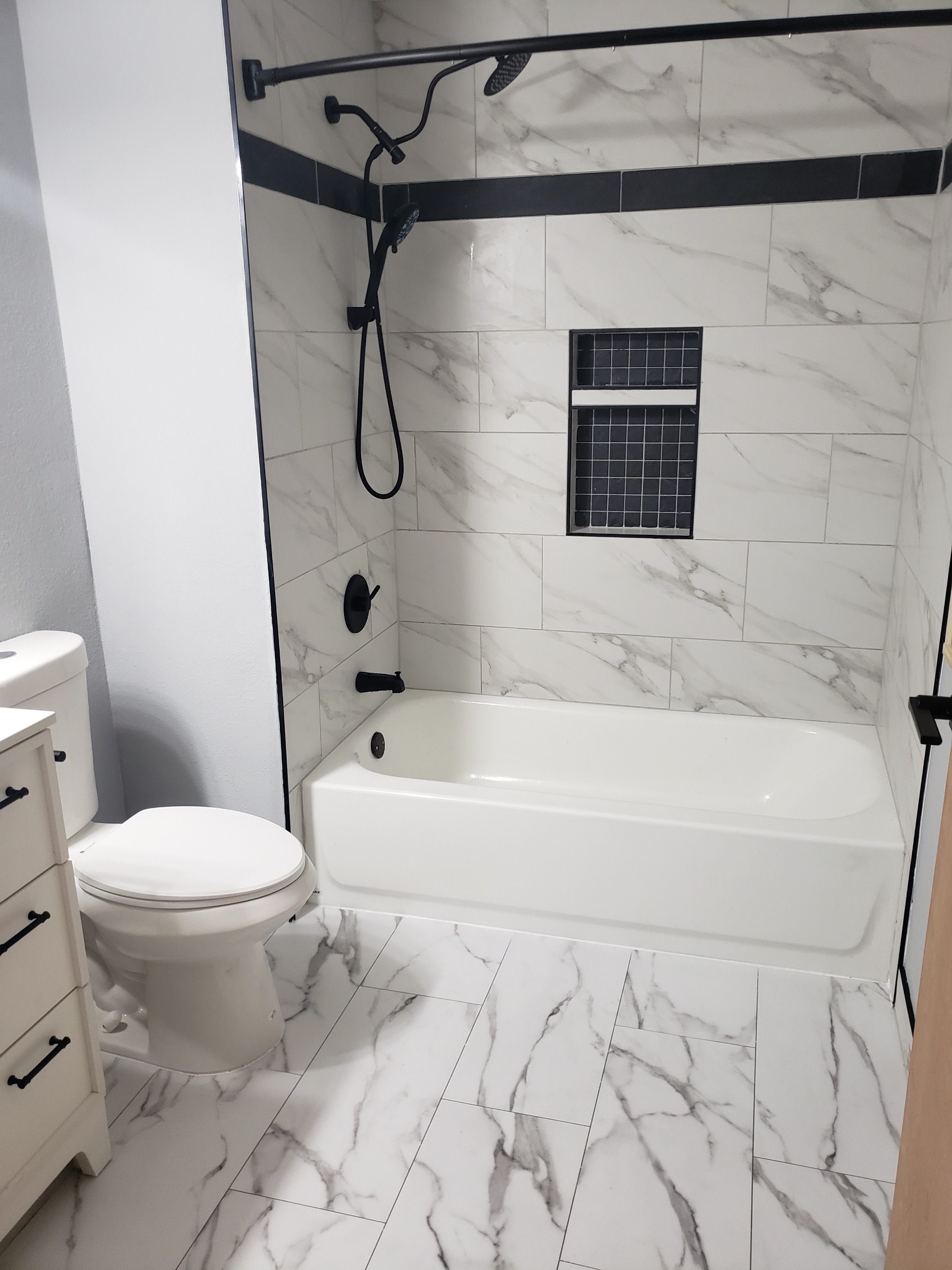 Finished bathroom after restoration — marble tile, matte black fixtures
