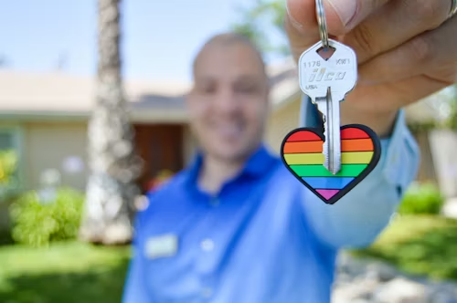 Man joyfully holding a house key decorated with a rainbow heart — representing homeownership for everyone