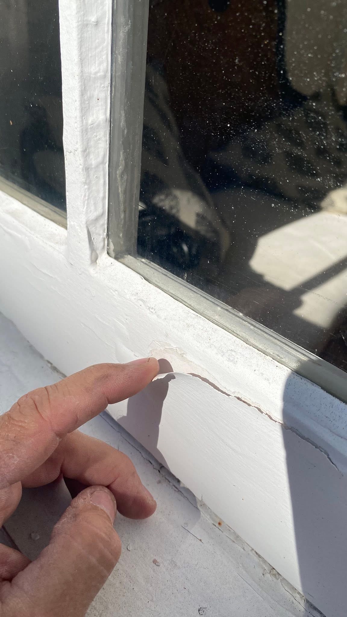 Paint peeling away from a wood window sill, exposing bare wood beneath