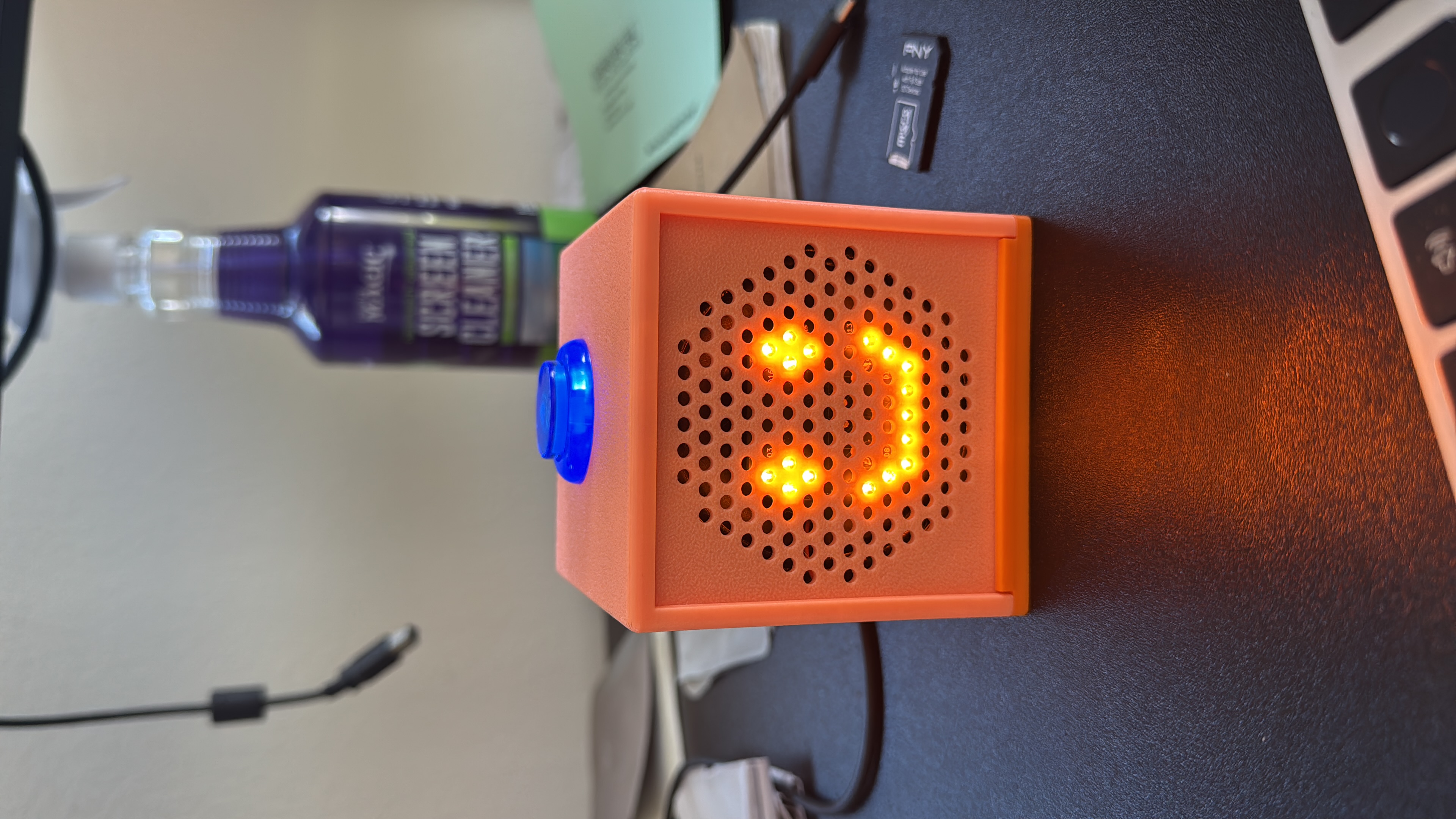 Grannybot device — orange cube with LED smiley face and blue button