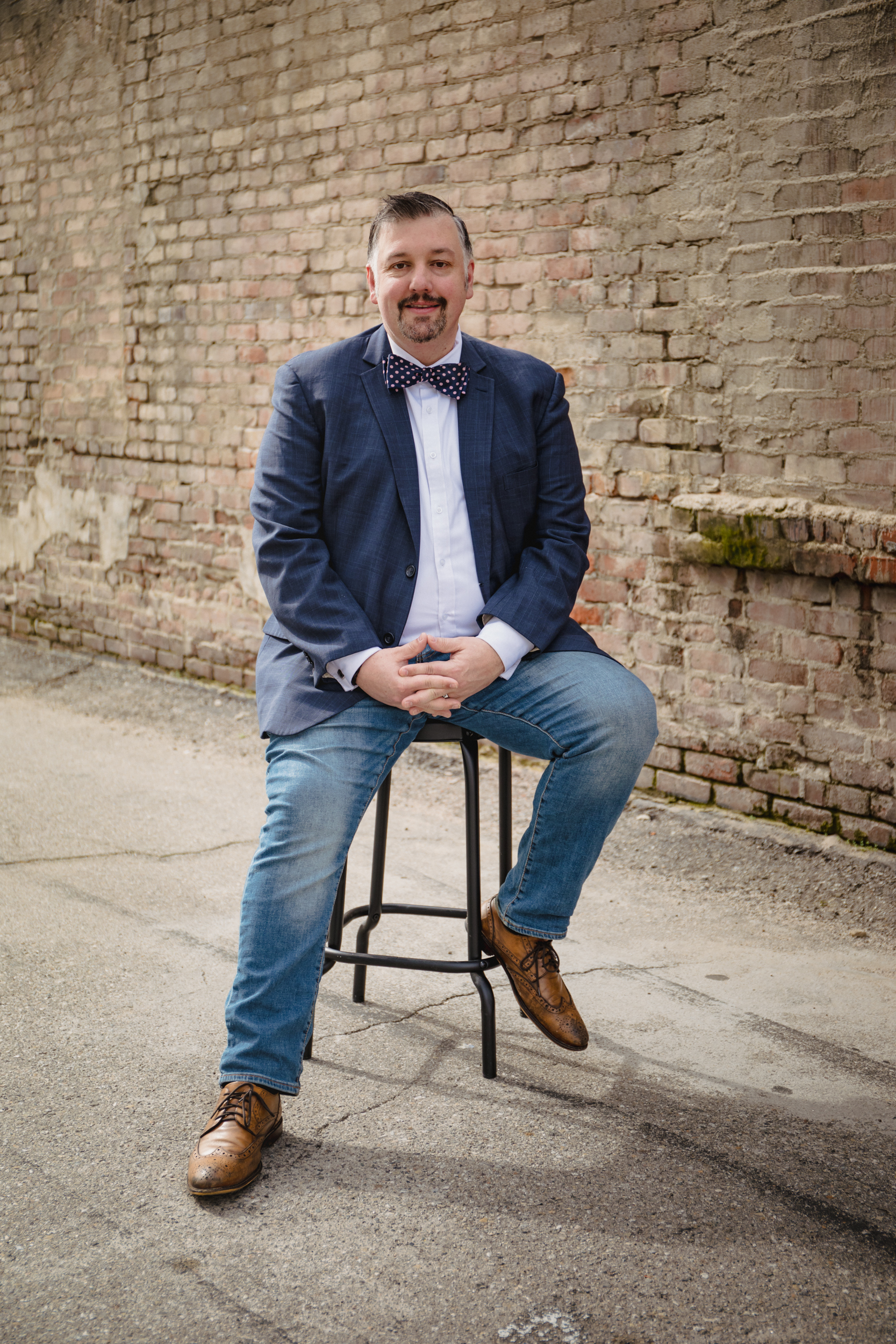 Tim McNeely — approachable full-body photo, blazer and jeans, brick wall background
