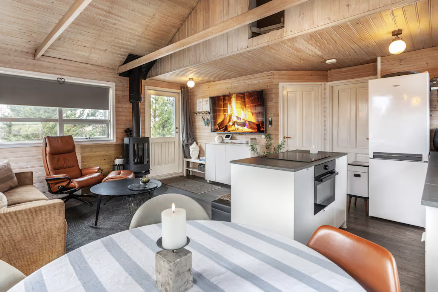 Warm timber living room and kitchen with a dining table, sofa and windows.