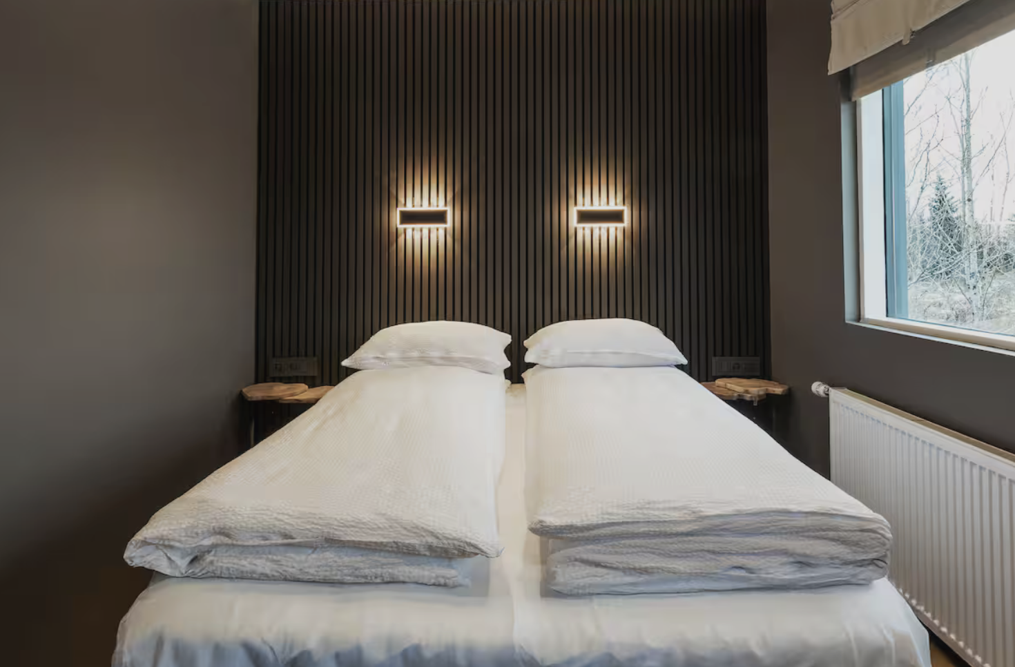 Bedroom with two single beds, a dark slatted wall and a window.