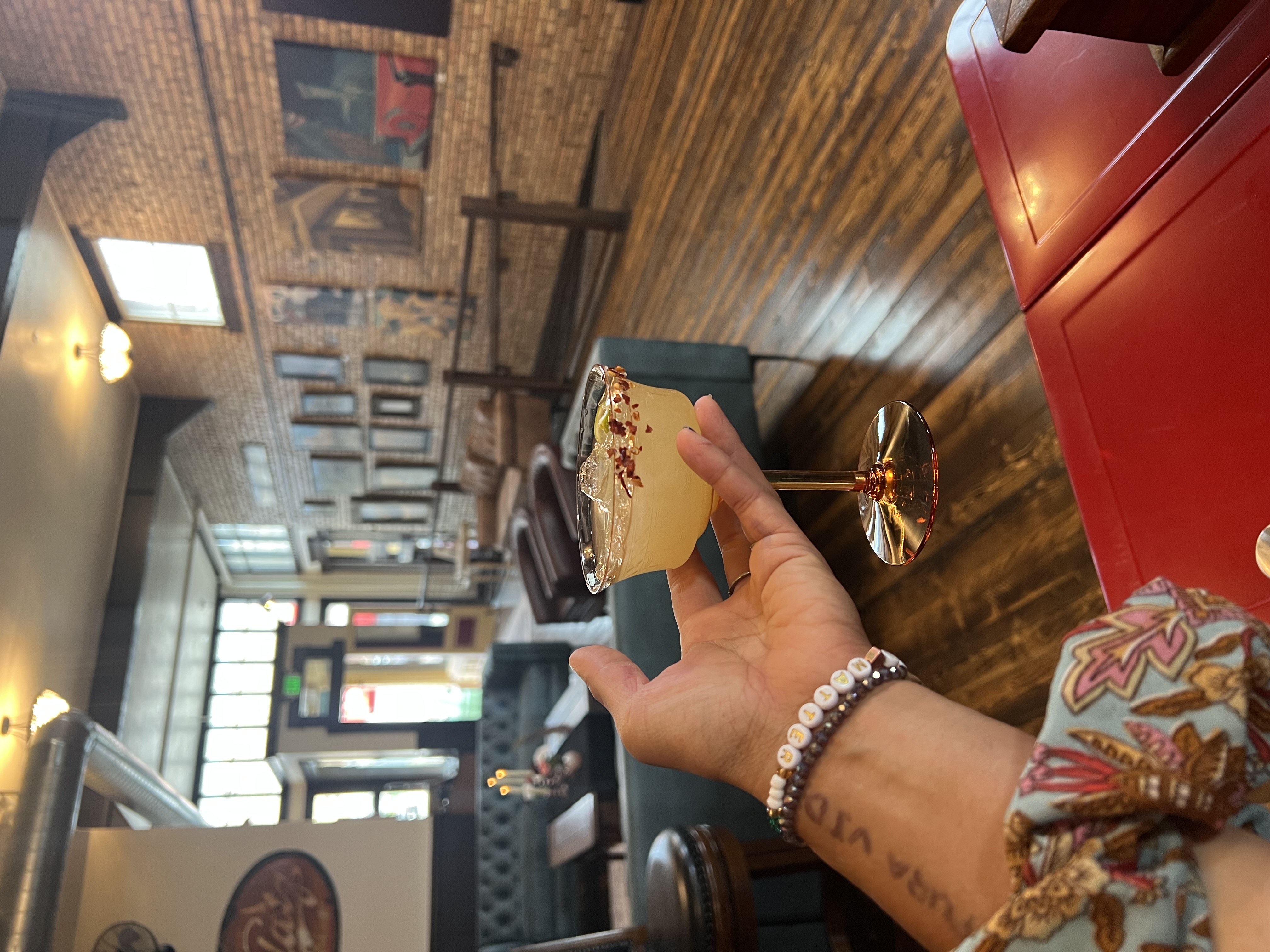 Nature's Rizz — hand holding coupe glass with golden drink, chili flakes on rim, saloon setting